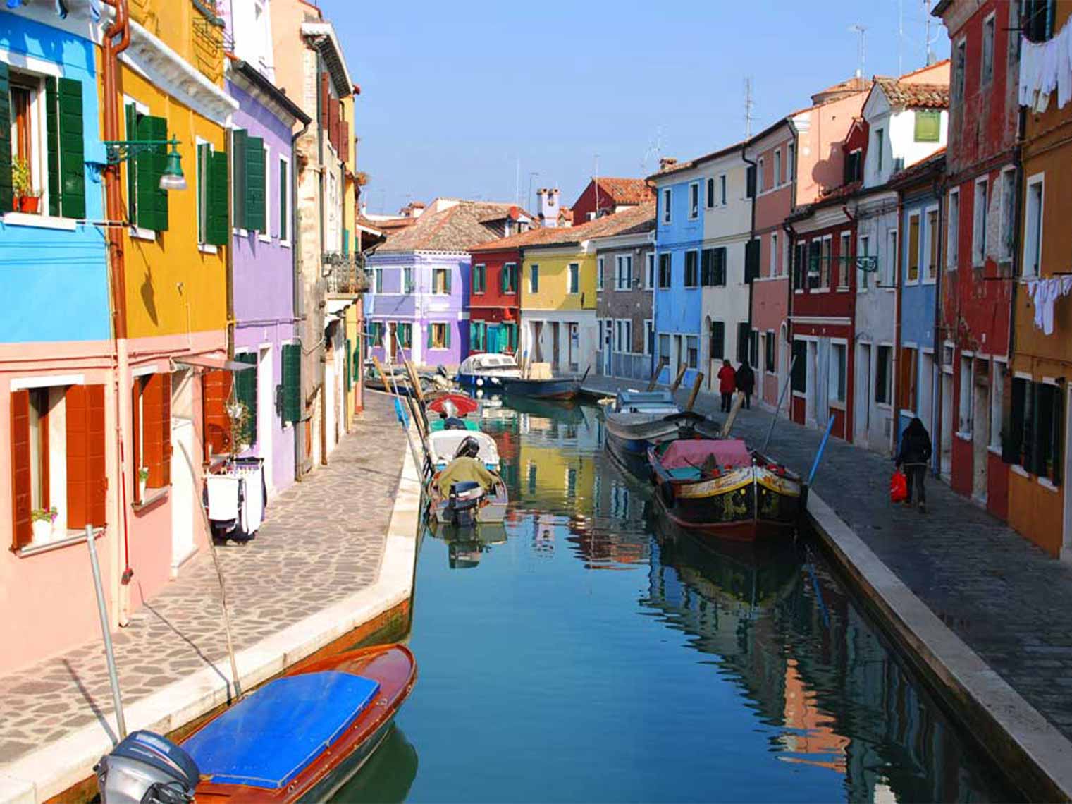 Colorful houses and boats lined up in the canal on a tour of Murano and Burano islands.