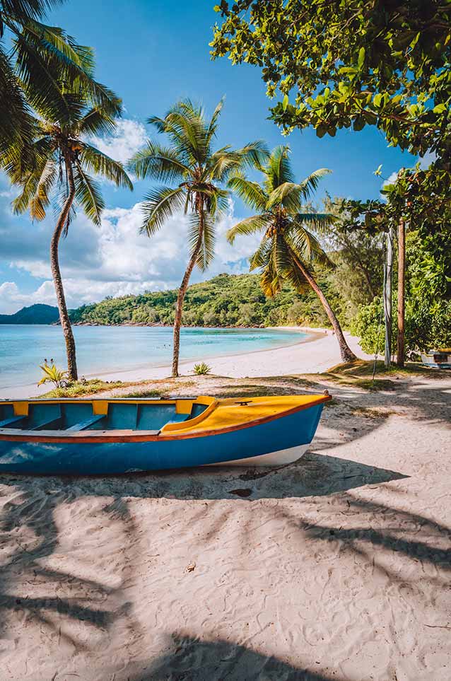 Mahe island, Seychelles. Local vivid colored boat under coconut palm trees on sunny day on shore of tropical beach