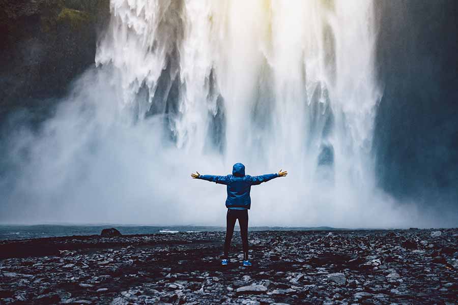 Woman in blue jacket standing at base of Skogafoss waterfall in Iceland