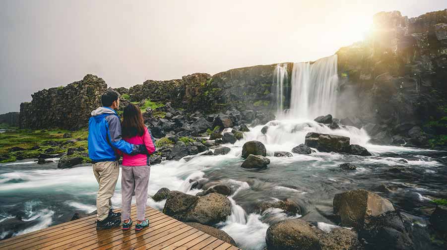 Young couple embracing looking onto waterfall at Thingvellir National Park, Iceland