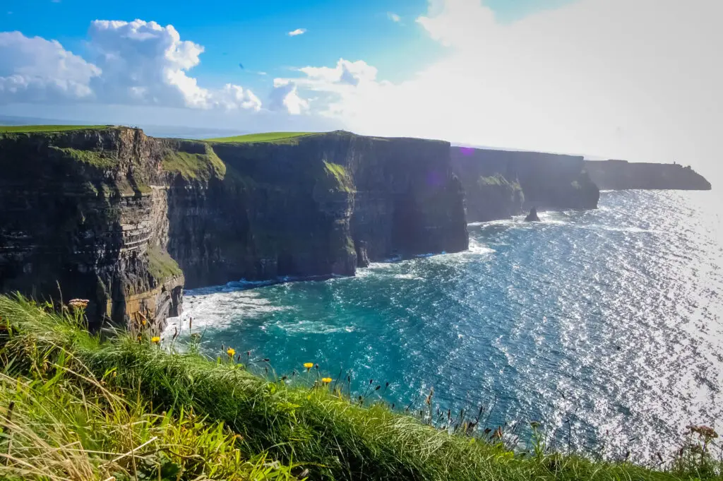 Breathtaking view of the Cliffs of Moher in Ireland, showcasing the lush greenery atop vertical sea cliffs under a clear blue sky.