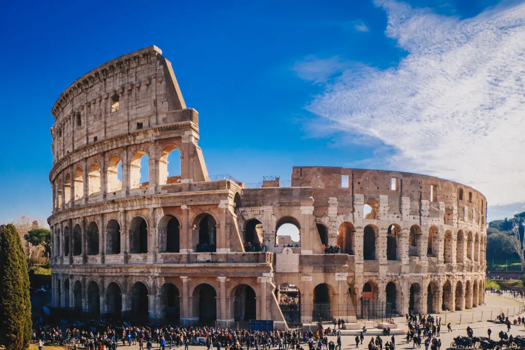 View of the iconic Colosseum in Rome, showcasing the exterior with bustling tourists under a clear blue sky.