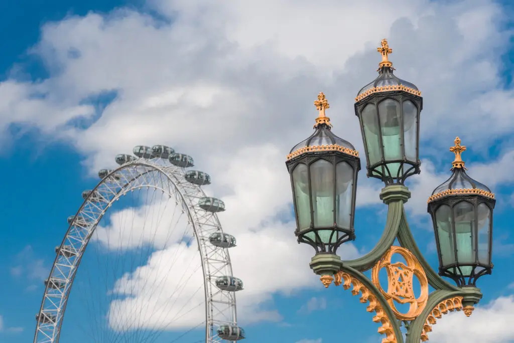 Elegant vintage lamp post on Westminster Bridge with the iconic London Eye in the background, under a partly cloudy sky in London, UK.