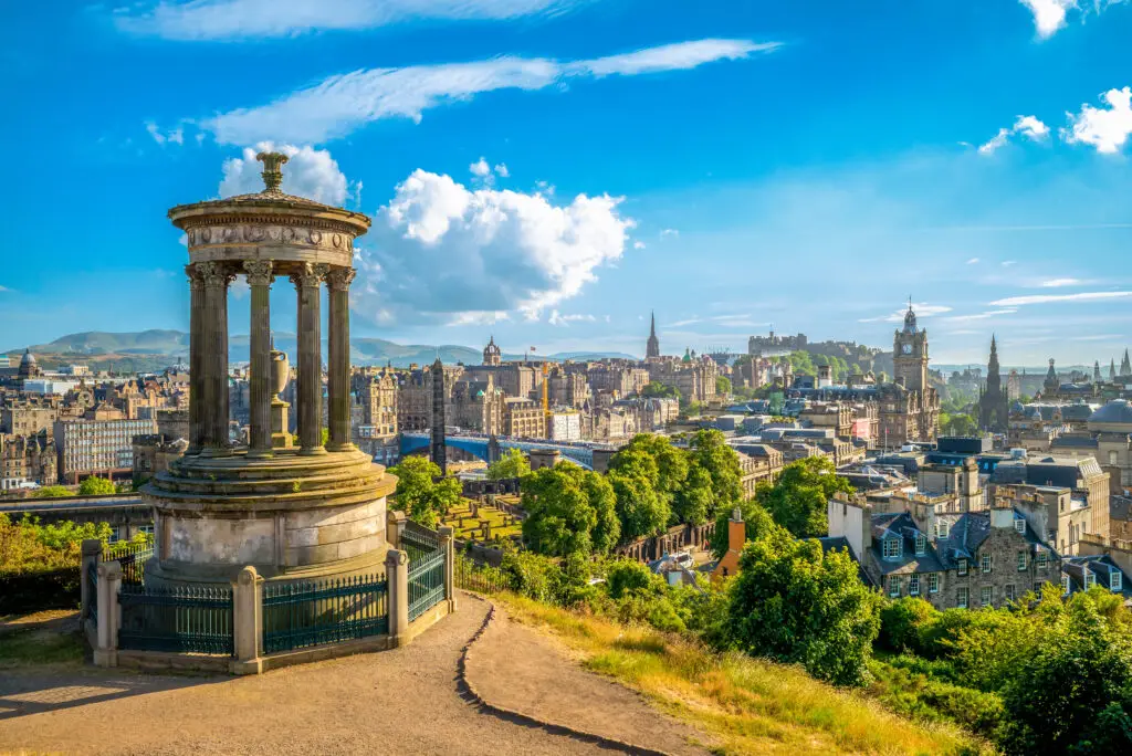 Panoramic view from Calton Hill in Edinburgh, UK, showcasing the Dugald Stewart Monument with the cityscape background on a bright sunny day.