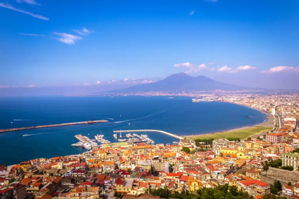 Aerial view of Naples with Mount Vesuvius in the background, showcasing the vibrant cityscape and beautiful coastline on a clear day.