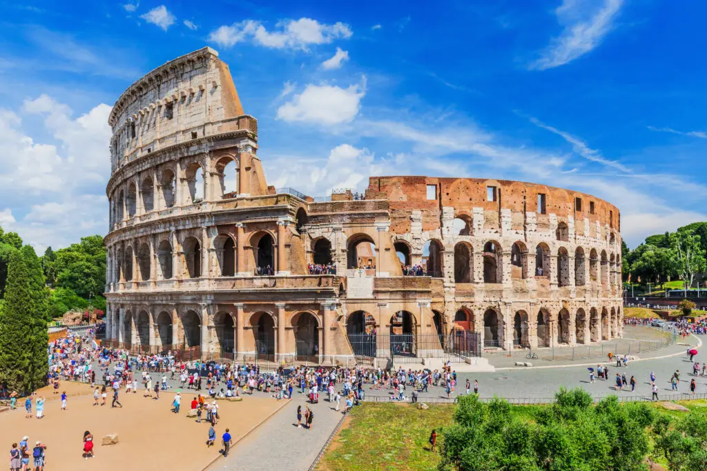 Vibrant view of the Colosseum in Rome, Italy, bustling with tourists under a clear blue sky.