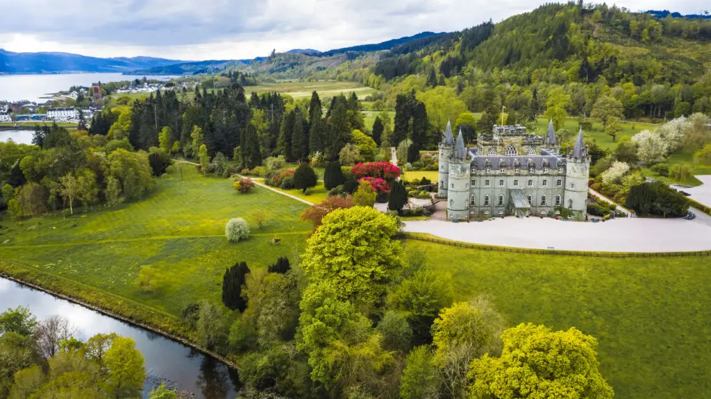 Aerial view of Inveraray Castle in Scotland surrounded by lush greenery and a scenic lake, showcasing historic architecture and vibrant landscapes.