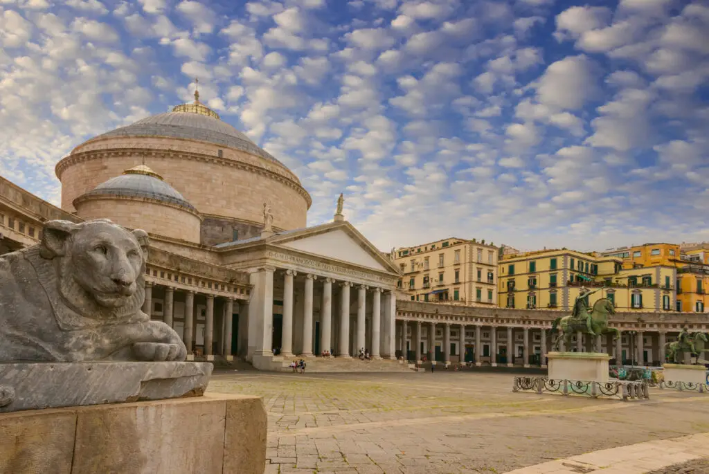 Exterior view of Basilica Reale Pontificia San Francesco da Paola on Piazza del Plebiscito in Naples, Italy, showcasing the church's neoclassical architecture and stone lion sculptures.