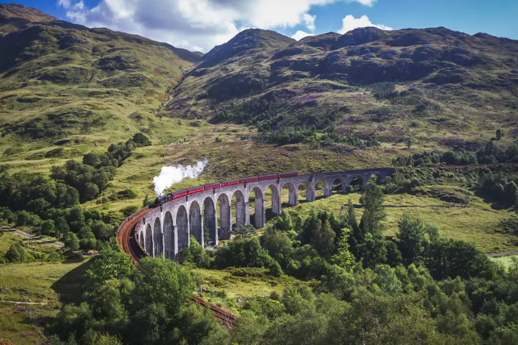 Jacobite steam train crossing the Glenfinnan Viaduct in Scotland, showcasing lush green landscapes and historic architecture.