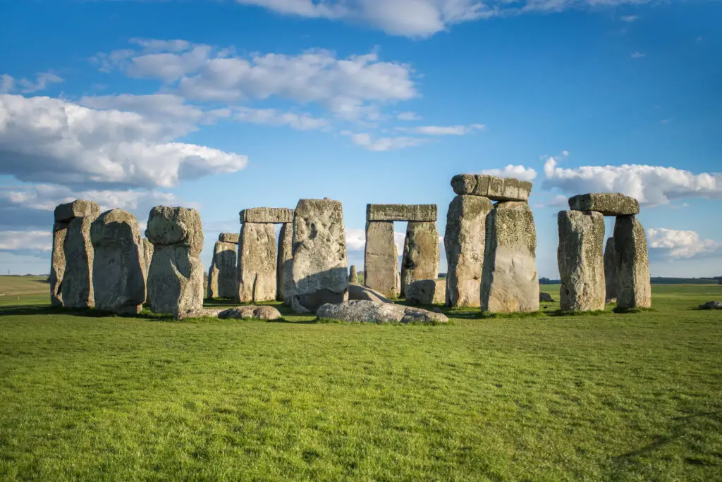 Stonehenge under clear skies: View of the ancient megalithic monument in Wiltshire, England, highlighting the stone circle set against a vibrant blue sky with scattered clouds.