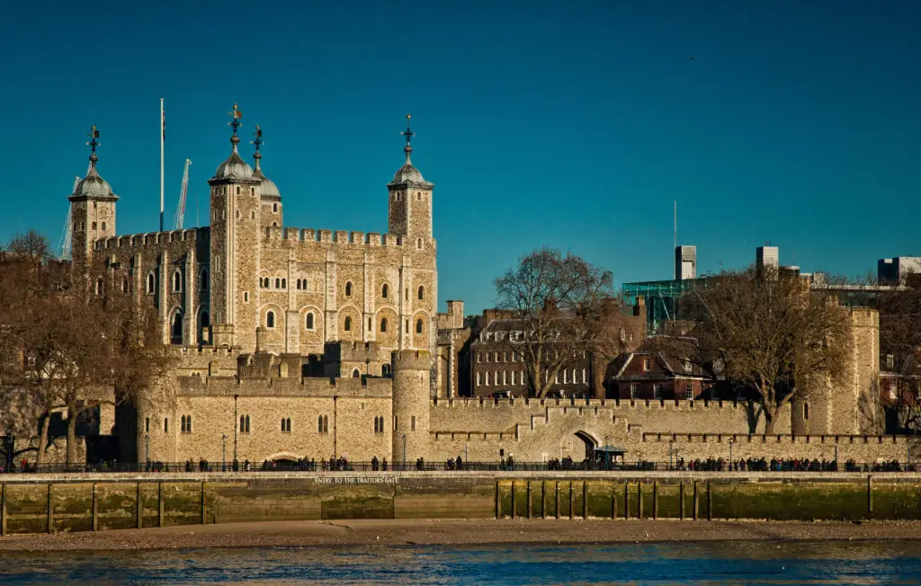 Sunny day view of the historic Tower of London, a prominent UNESCO World Heritage Site, showing its iconic stone walls and towers against a clear blue sky.
