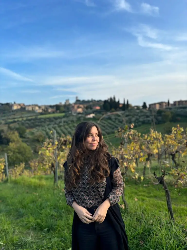 Young woman enjoying a serene Tuscan landscape, with historic village and vineyards in the background, promoting travel in Italy.