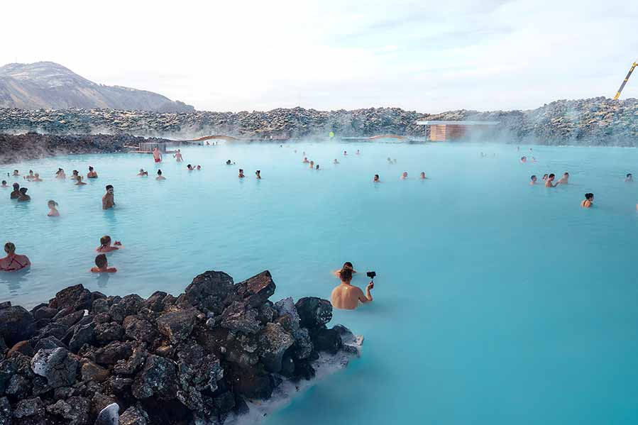 Tourists enjoying a serene soak in the milky blue waters of Blue Lagoon, Iceland, surrounded by rugged lava fields.