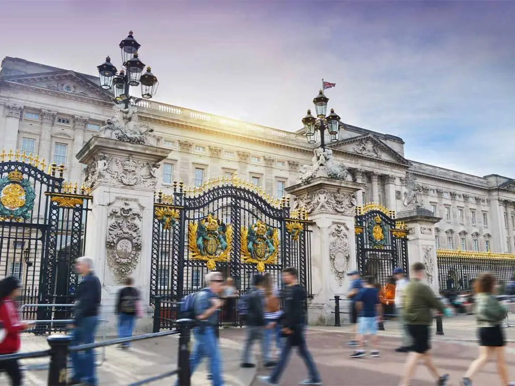 Tourists walking in front of the majestic Buckingham Palace gates during a sunny day in London, England
