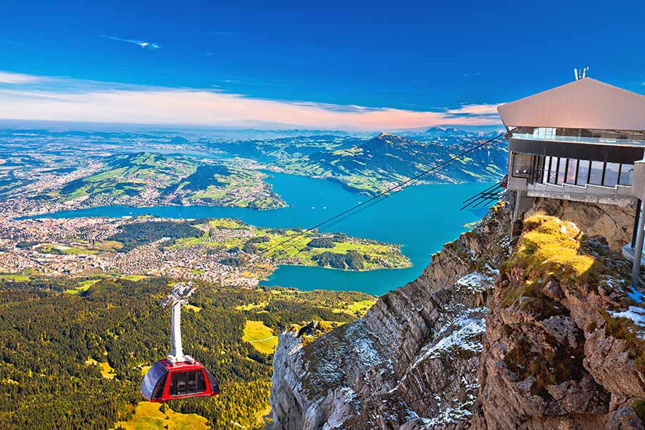 Scenic view from Mount Pilatus featuring a cable car ascending with panoramic sights of Lucerne, Switzerland, highlighting the outdoor tourism experience in the Swiss Alps.