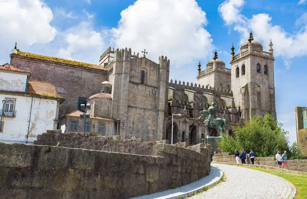 View of the historic Sé do Porto Cathedral and statue of Vimara Peres under a clear blue sky, with tourists exploring the site, in Porto, Portugal.