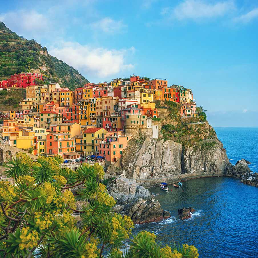 Vibrant houses stacked on steep cliffs overlooking a serene bay in Cinque Terre, Liguria, Italy, showcasing the unique architecture and picturesque coastal scenery of the region.