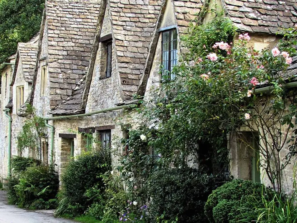 Charming old stone cottages with climbing roses in the Cotswolds, England, depicting traditional British architecture and lush gardens.