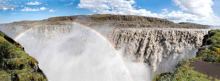 Panoramic view of Dettifoss Falls in Iceland with a vivid rainbow over the misty waters