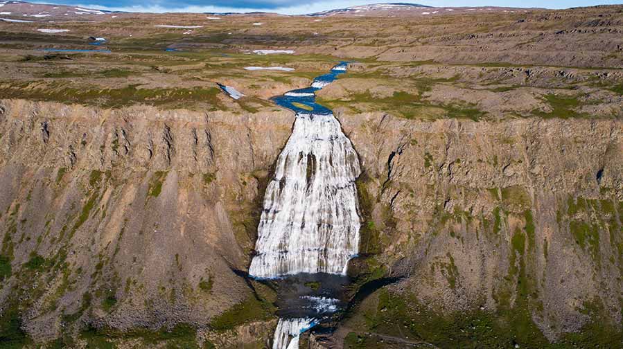 Aerial view of the majestic Dynjandi Waterfall cascading down rugged cliffs in the Westfjords of Iceland, showcasing the stunning natural landscape.
