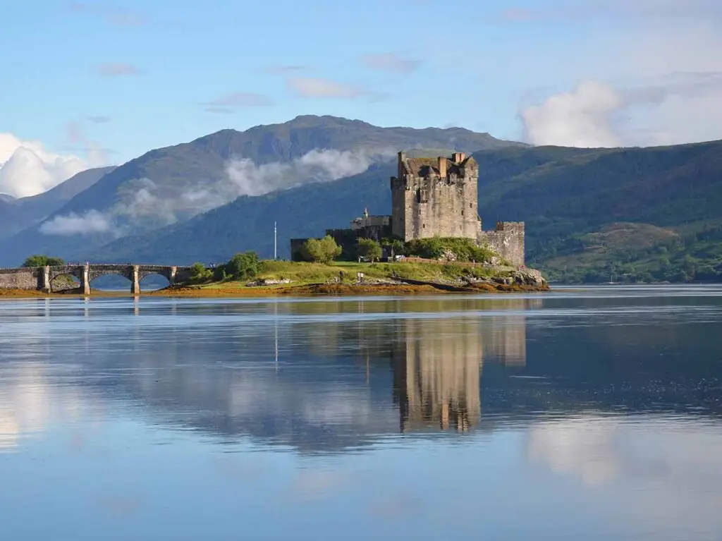 Eilean Donan Castle reflecting on the calm waters of Loch Duich in the Scottish Highlands on a clear day.