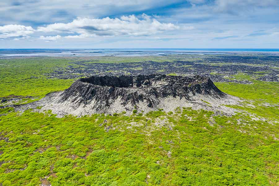 Aerial view of Eldborg Crater in Iceland, showcasing its distinctive volcanic structure surrounded by lush greenery and expansive flat landscapes.