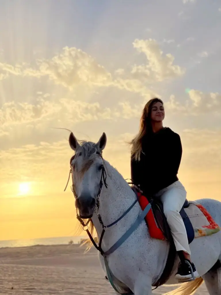 Woman enjoying a sunset horseback ride on a sandy beach in Morocco