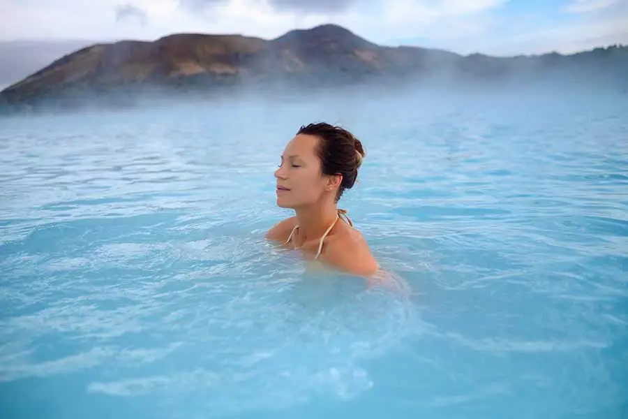 Woman relaxing in the Blue Lagoon, a serene geothermal spa in Iceland, with misty mountains in the background.