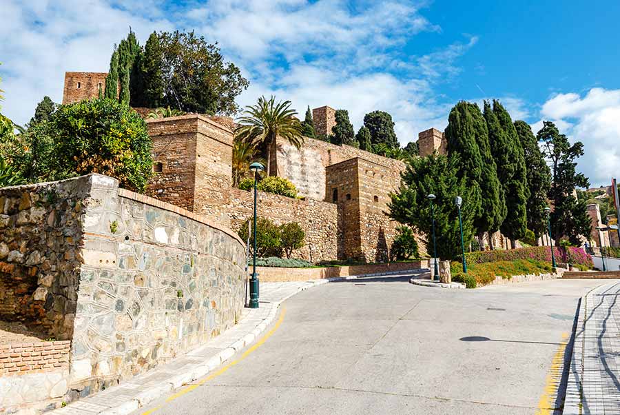 Sunny view of the historic Gibralfaro Castle in Malaga, Spain, with surrounding lush greenery and clear blue sky.