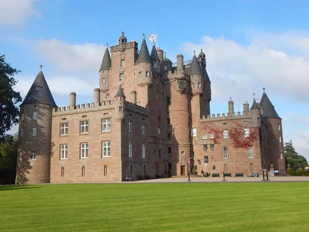 Glamis Castle in Scotland with lush green lawns under a clear blue sky, a must-visit historic tourist attraction featured on Travel by Luxe.