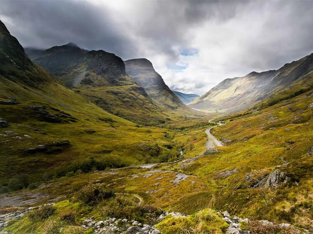 Breathtaking view of Glencoe Valley in Scotland with lush greenery and dramatic mountain peaks under a cloudy sky