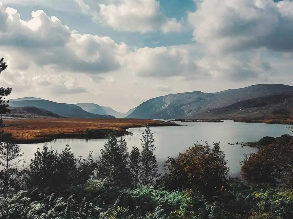 Scenic view of Glenveagh National Park in Ireland, featuring serene waters, rolling hills, and lush greenery under a cloudy sky.