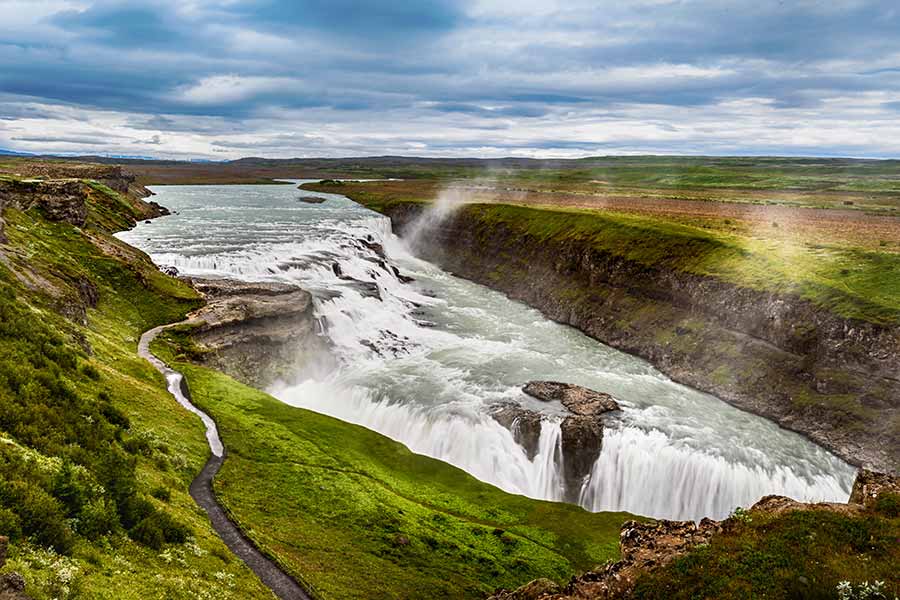 Panoramic view of Gullfoss Waterfall in Iceland, showcasing the majestic cascades and green landscapes surrounding it.
