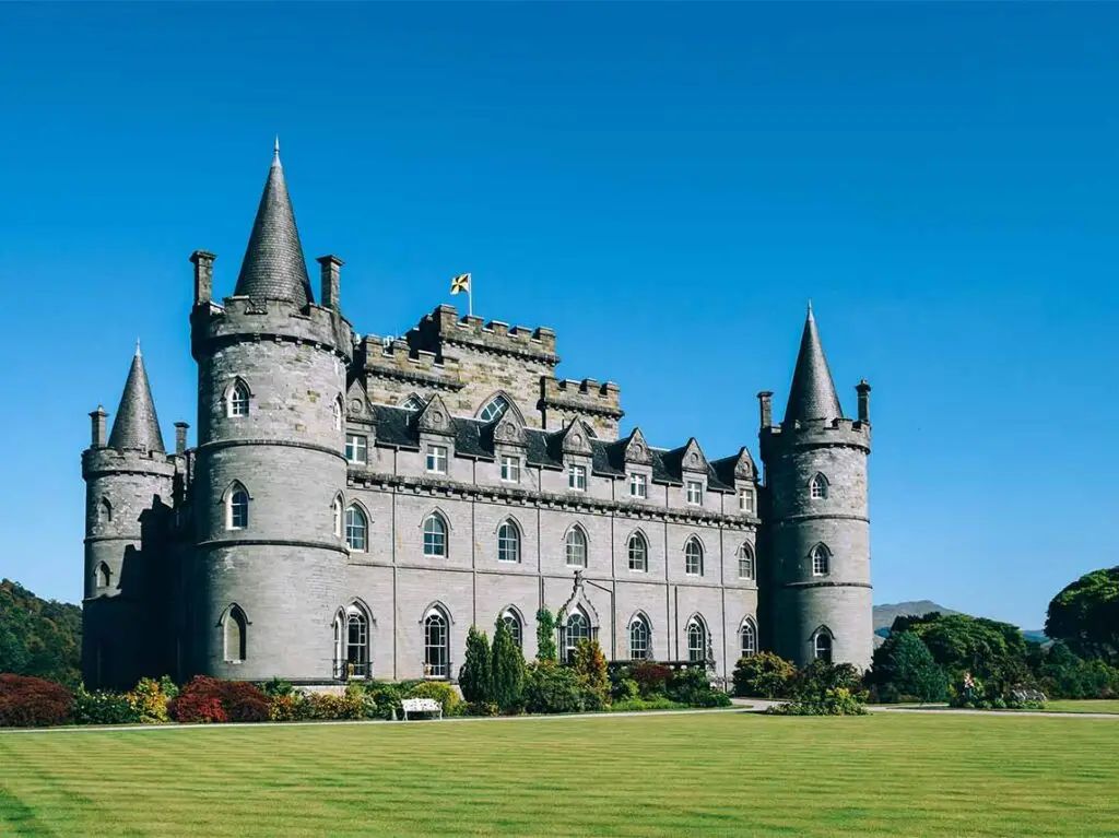Majestic Inveraray Castle surrounded by lush greenery under a clear blue sky in Scotland, a prime example of historic Scottish architecture and a popular tourist attraction.