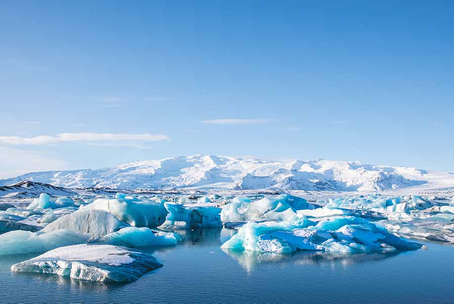 Scenic view of Jokulsarlon Glacier Lagoon in Iceland, featuring vibrant blue icebergs and snow-capped mountains under a clear sky.