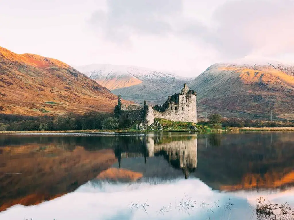 Majestic view of Kilchurn Castle in Scotland with reflections on Loch Awe and surrounded by scenic autumn-colored mountains