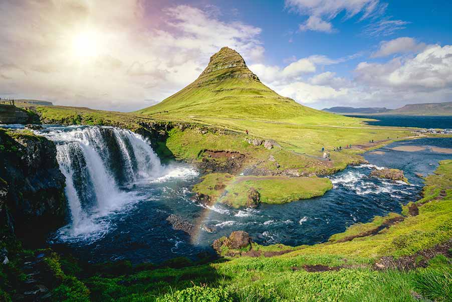 Scenic view of Kirkjufell mountain and waterfall in Iceland, showcasing vibrant green landscapes and a flowing river under a clear sky.