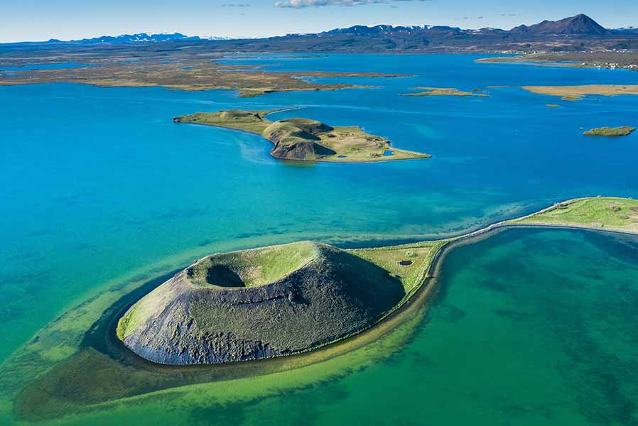 Aerial view of Lake Myvatn in Iceland, showcasing vibrant blue waters, unique volcanic formations, and lush green surroundings.