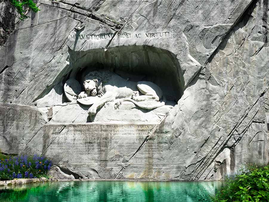 Carved image of the Lion Monument in Lucerne, Switzerland, depicting a dying lion in a rock with a pond in front and surrounded by greenery.