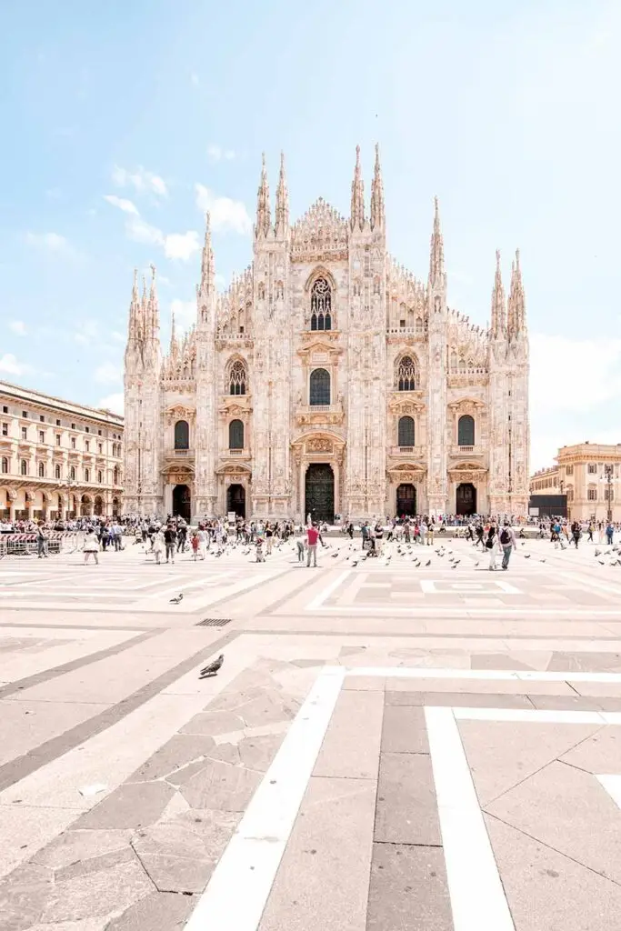 Bright and detailed view of Milan Cathedral's intricate facade with tourists and pigeons on the sunny Piazza del Duomo, Italy