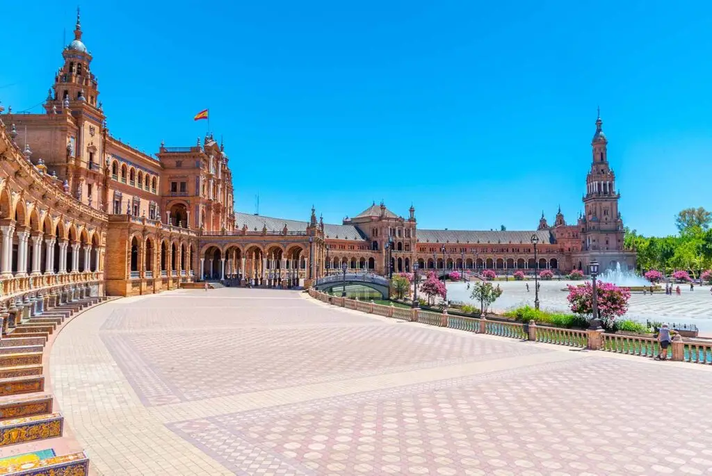 Bright sunny view of Plaza de España in Seville, Spain, showcasing the intricate architecture and expansive courtyard with a clear blue sky.