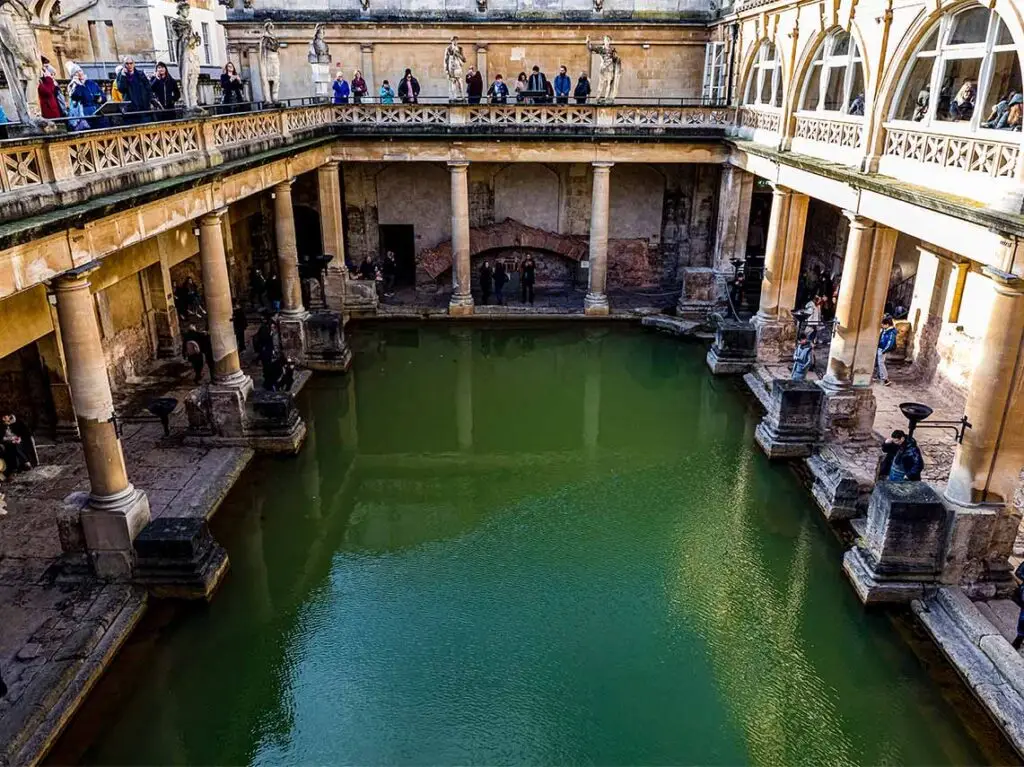 Visitors exploring the ancient Roman Baths in Bath, England, showcasing the historical architecture and green thermal waters.