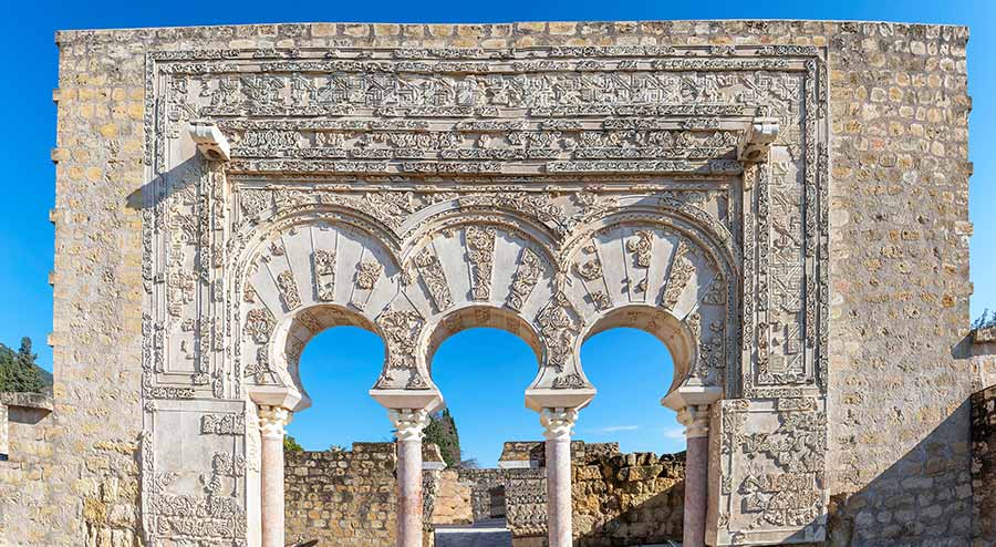 Detailed view of the ornately carved arches at the ruins of Medina Azahara in Cordoba, Spain, showcasing Islamic art and architecture under a clear blue sky