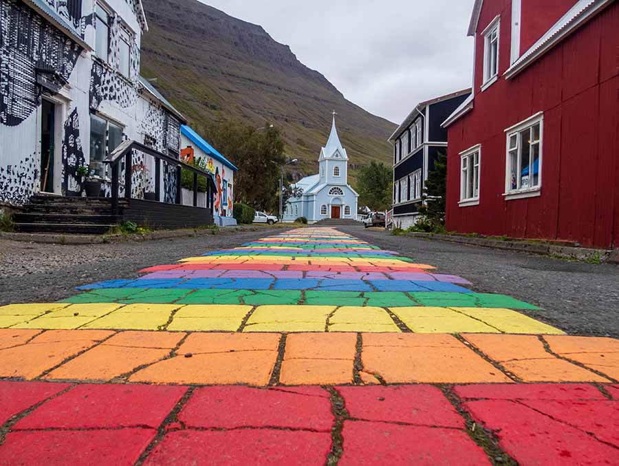 Colorful cobblestone street leading to a charming white church in the picturesque village of Seydisfjordur, Iceland, surrounded by mountains and colorful buildings.
