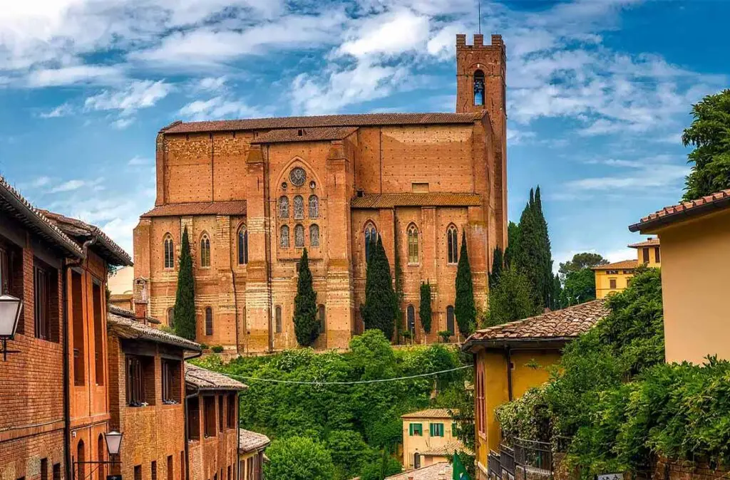 Scenic view of the historic San Domenico Basilica set against a blue sky in Siena, Italy, surrounded by traditional Tuscan houses.