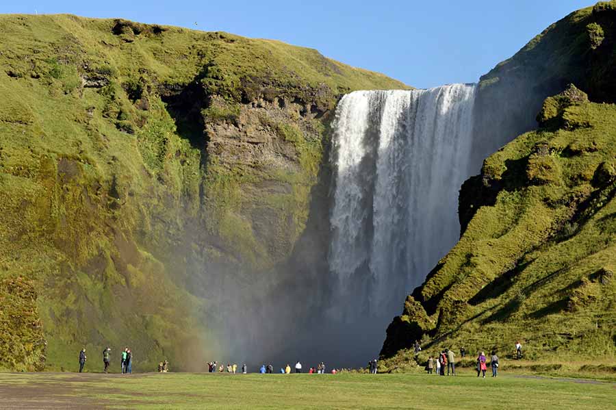 Skogafoss Waterfall in Iceland, a majestic tourist attraction with visitors admiring the powerful cascade and vibrant green landscapes.