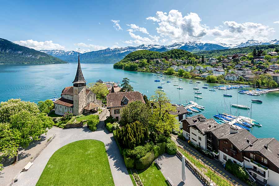 Scenic view of Spiez Castle with surrounding village and Lake Thun in Bern, Switzerland, showcasing lush greenery and Alpine mountains in the background