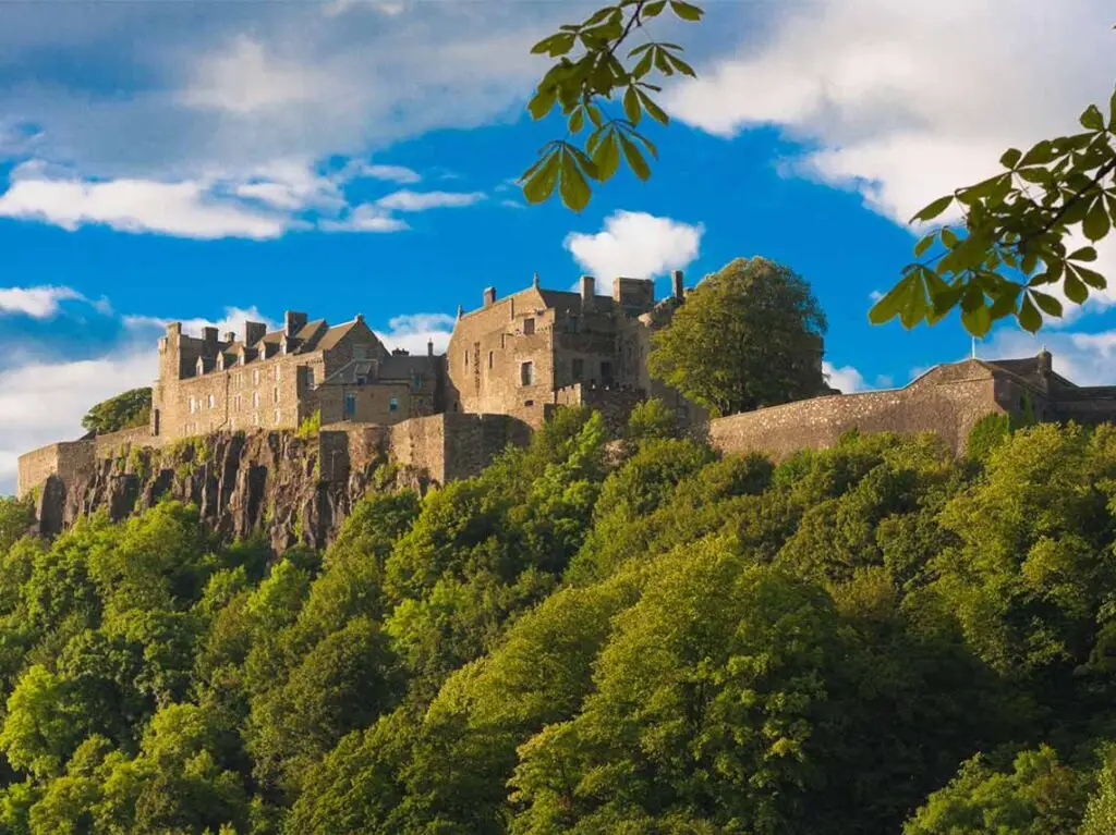 Majestic view of Stirling Castle perched on a rocky cliff surrounded by lush greenery under a bright blue sky in Scotland, a popular historical tourist destination.