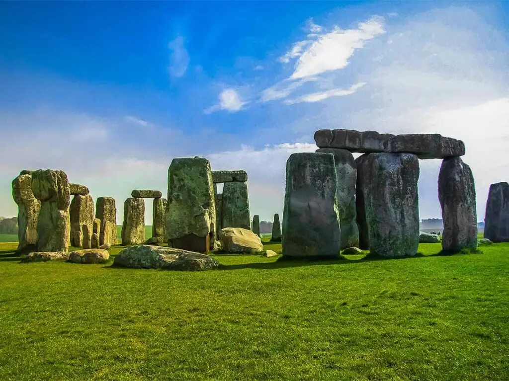 Panoramic view of Stonehenge under a blue sky, showcasing the ancient and mysterious circle of standing stones on the lush green plains of England.