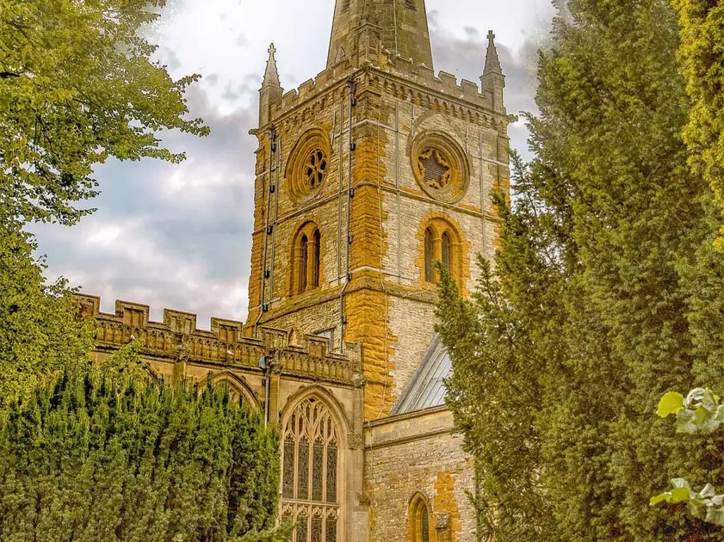 Stratford-upon-Avon's Holy Trinity Church surrounded by lush greenery, a popular historical tourist attraction in England.